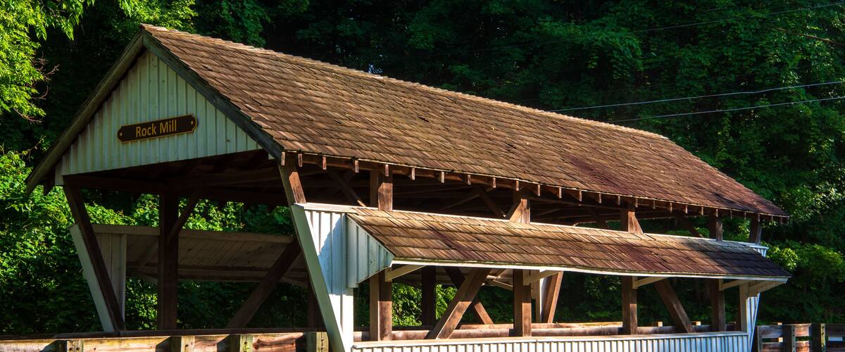 A rustic wooden structure labeled 'Rock Mill' with a metal roof, surrounded by lush greenery.