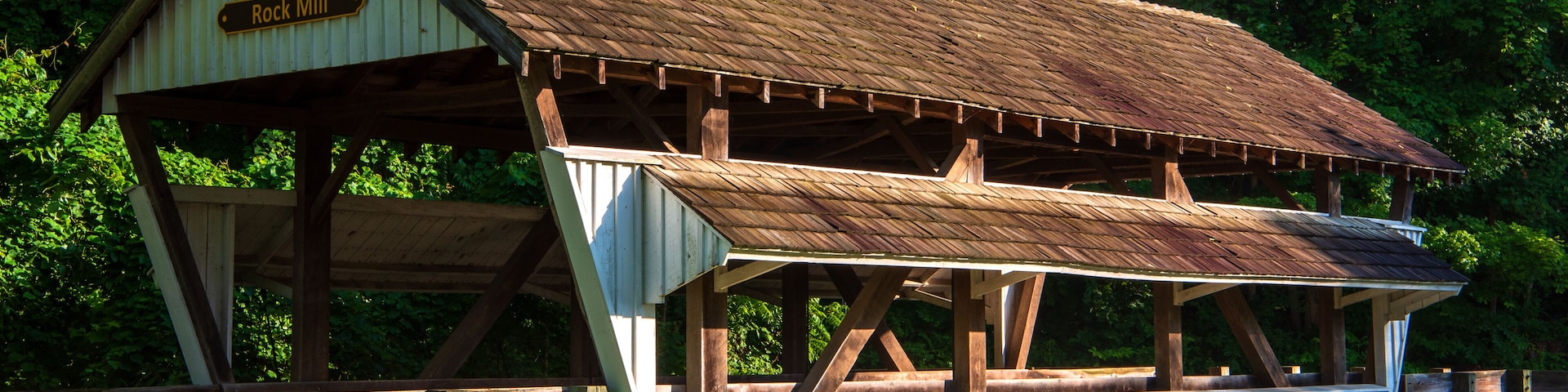 A rustic wooden structure labeled 'Rock Mill' with a metal roof, surrounded by lush greenery.