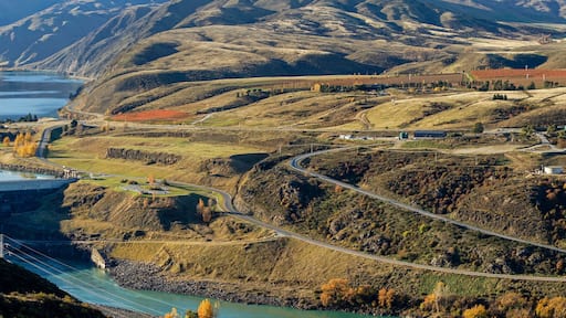 Panoramic aerial view to Clyde dam with river and winding road on hillside surrounded by mountainous and autumn trees.