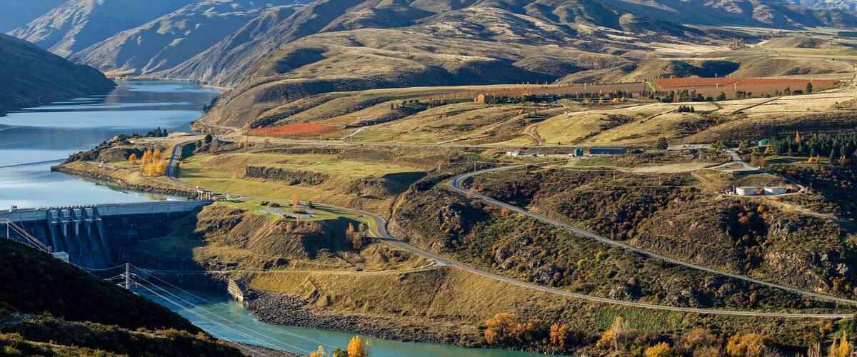 A dam, a winding road, and a river in a mountainous landscape.