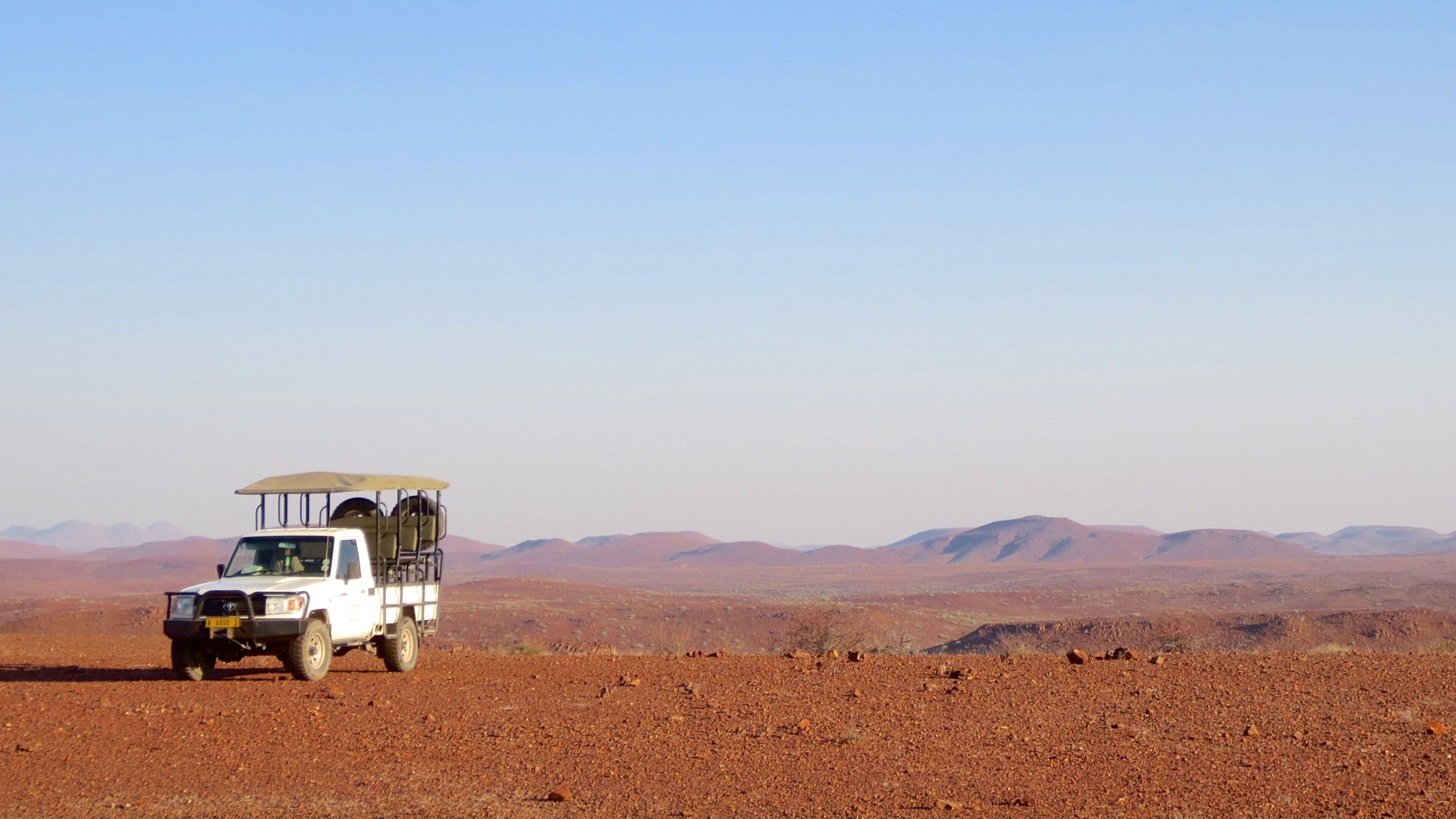 A white safari vehicle with a roof and four seats parked on a barren, rocky landscape with distant mountains.