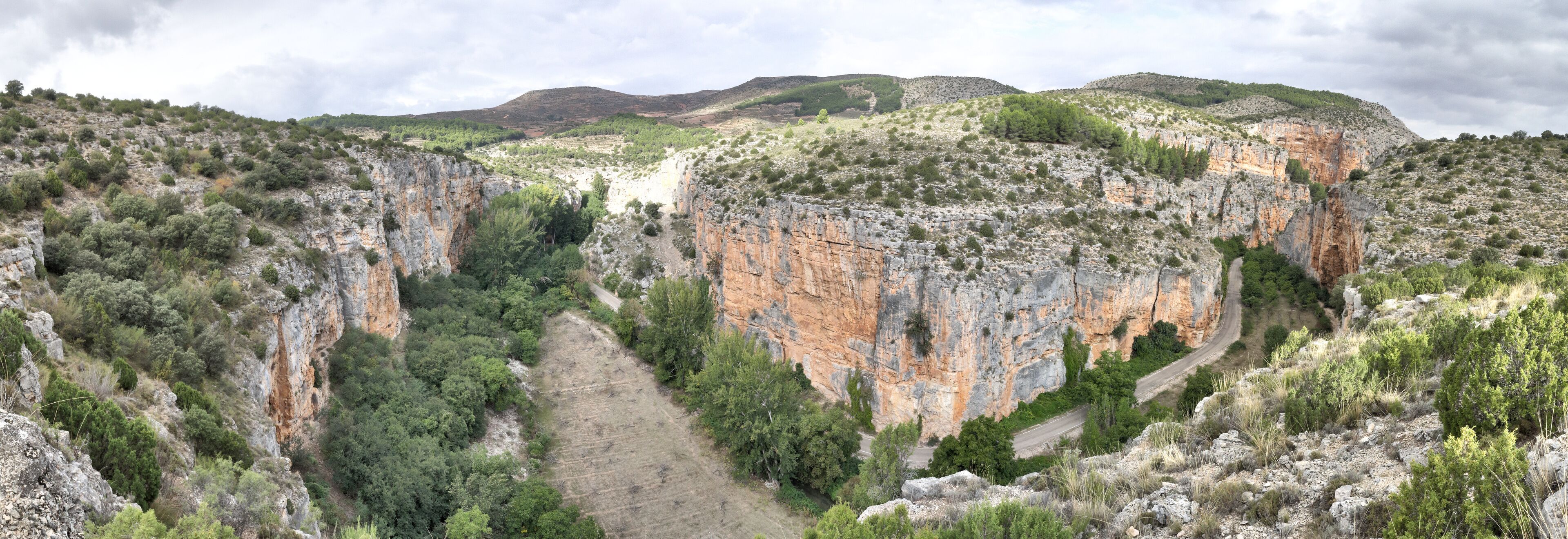 A rugged canyon with steep cliffs, a winding road, and sparse vegetation.
