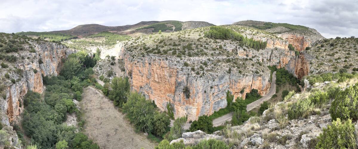 A rugged canyon with steep cliffs, a winding road, and sparse vegetation.