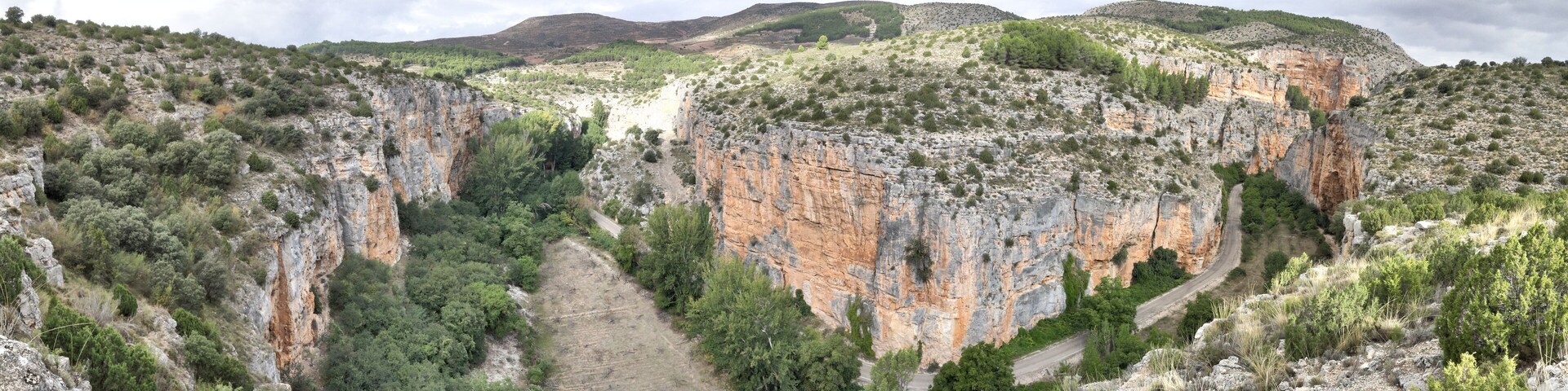 A rugged canyon with steep cliffs, a winding road, and sparse vegetation.
