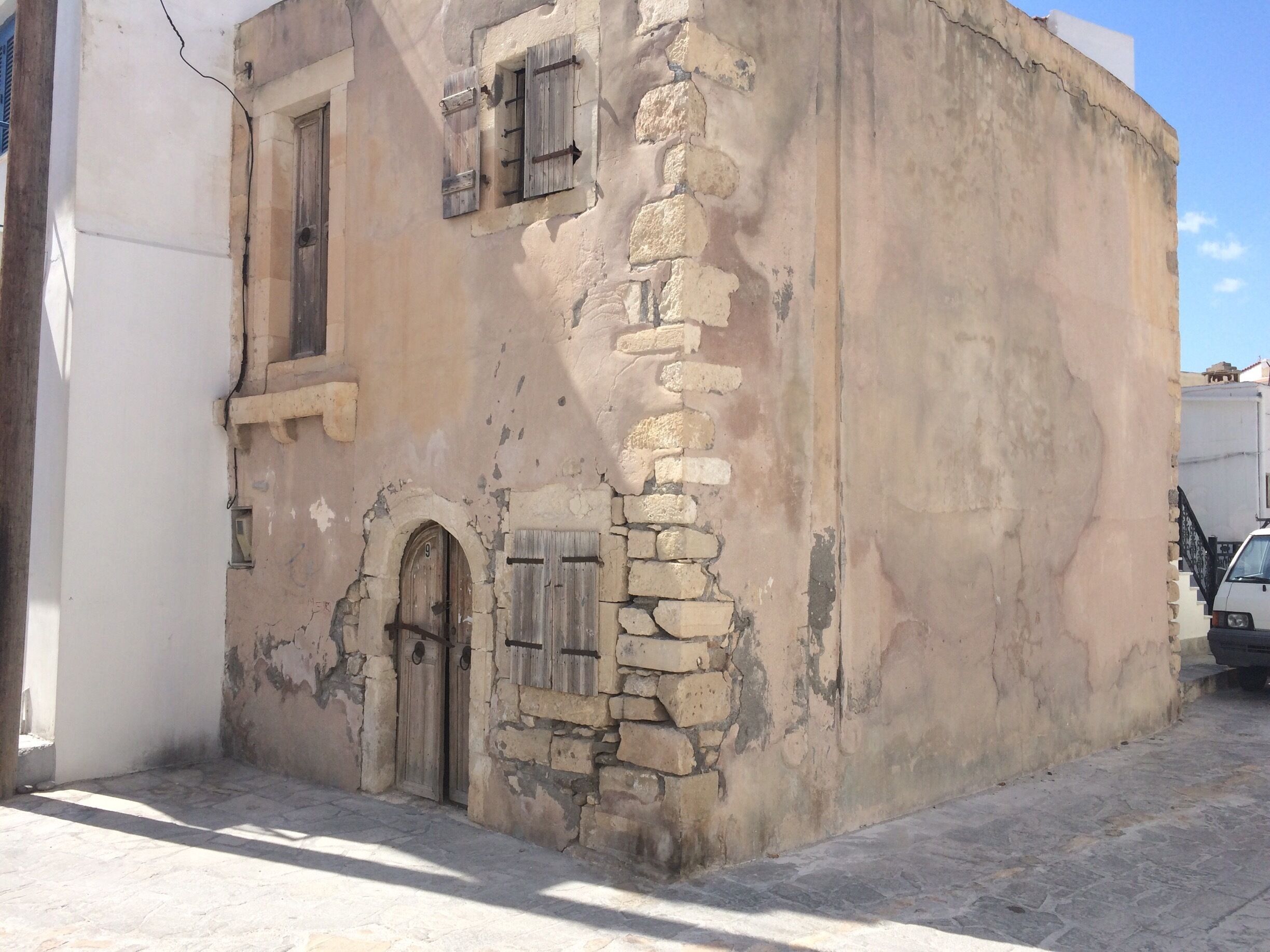 A weathered building with stone walls, wooden shutters, and a single arched door.