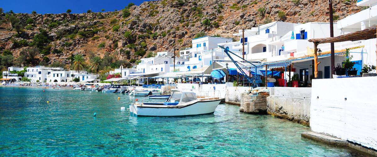 A coastal town with white buildings, clear turquoise water, and rocky hills in the background.