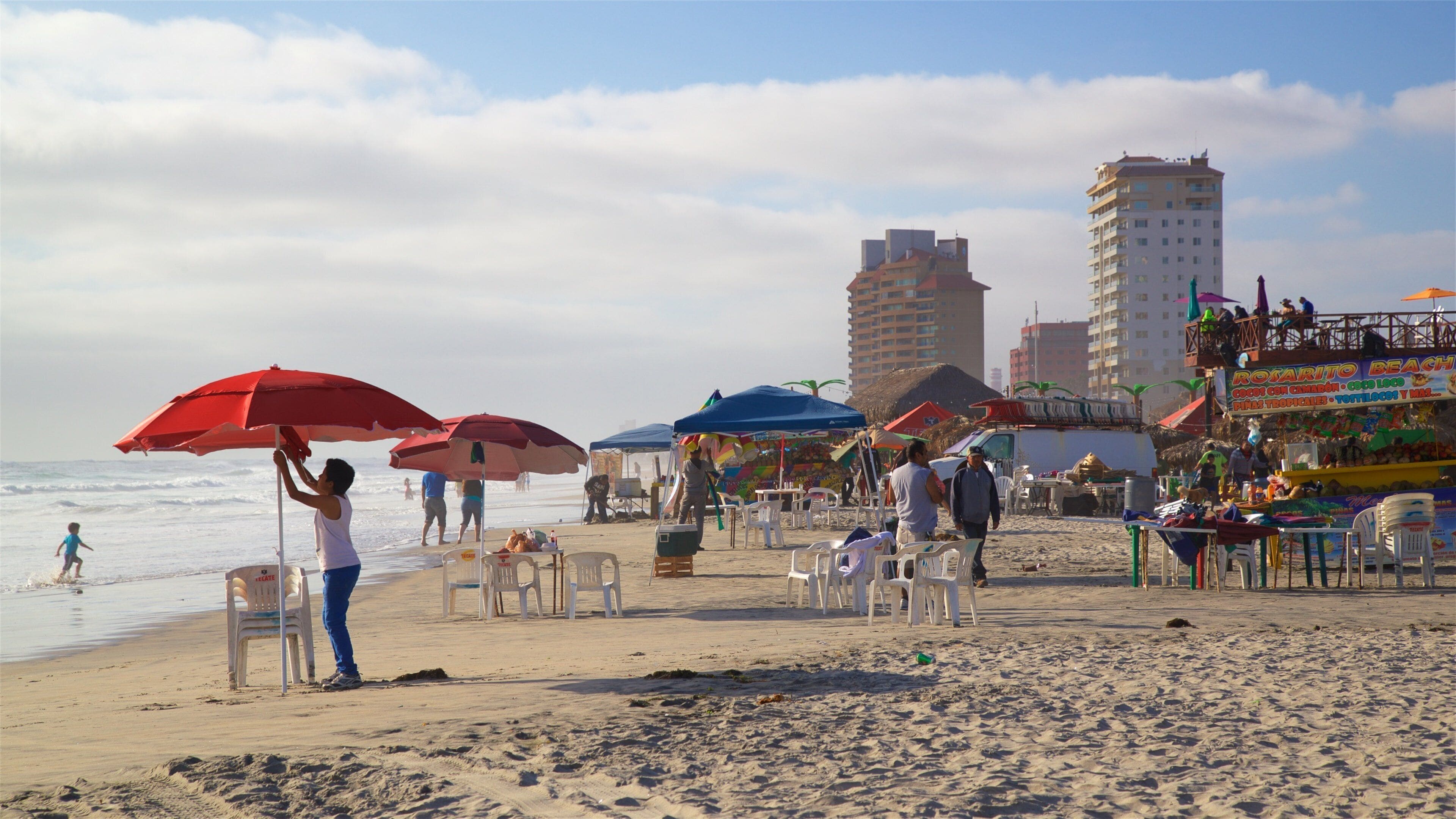A beach with umbrellas, chairs, and people.