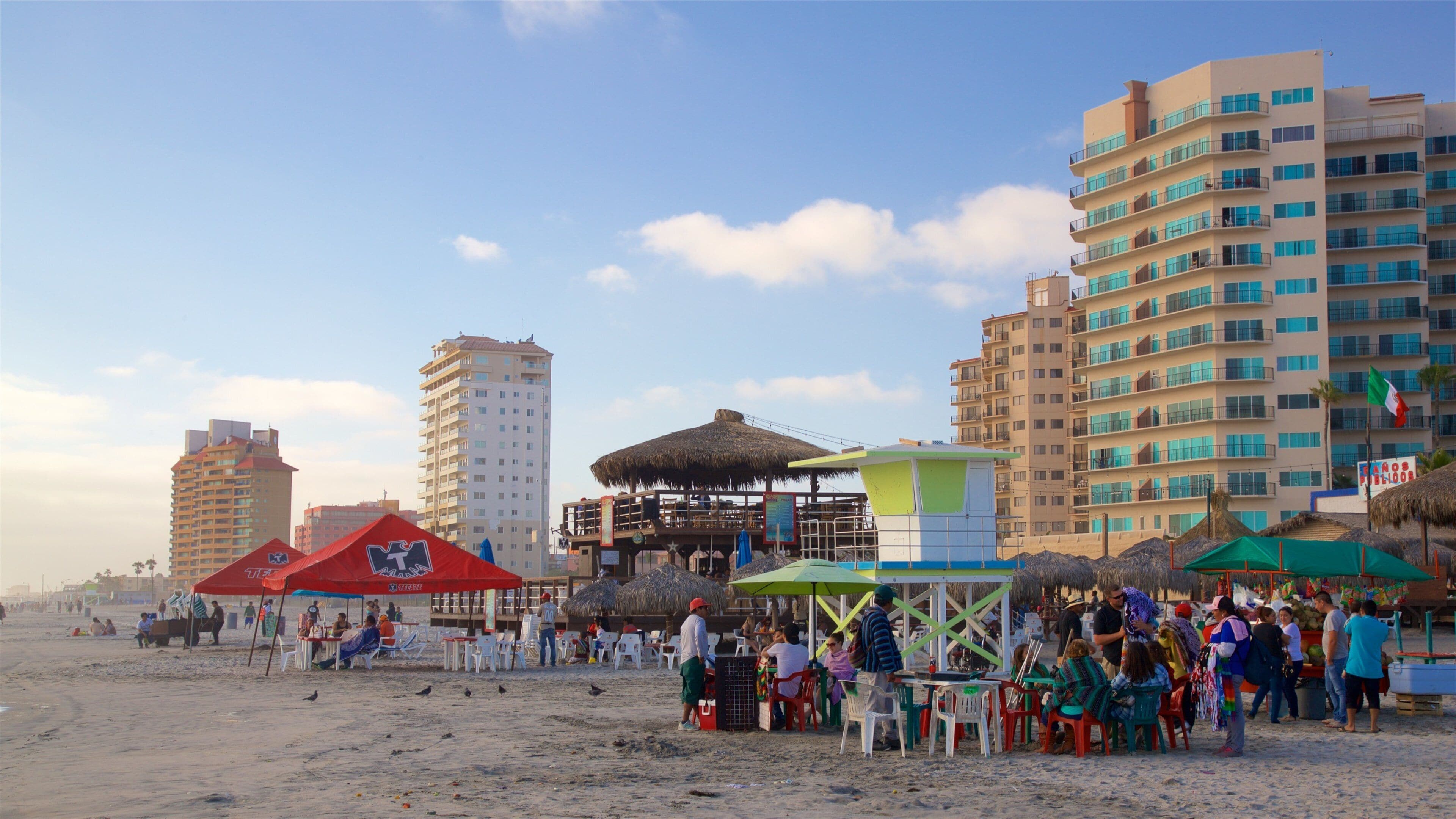 A beach with people, a lifeguard tower, and tall buildings in the background.