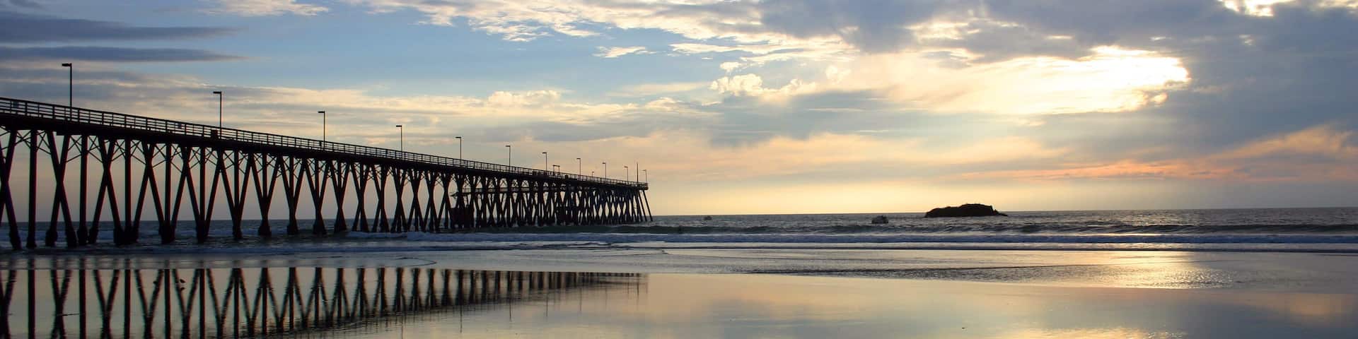 A pier extending into the ocean with a sunset in the background.