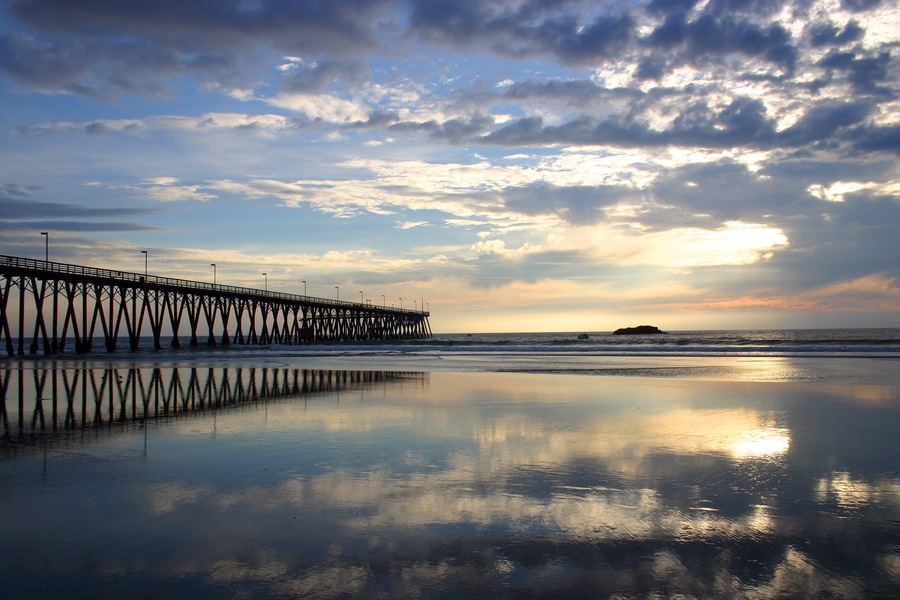 Un muelle que se adentra en el océano con un atardecer de fondo.