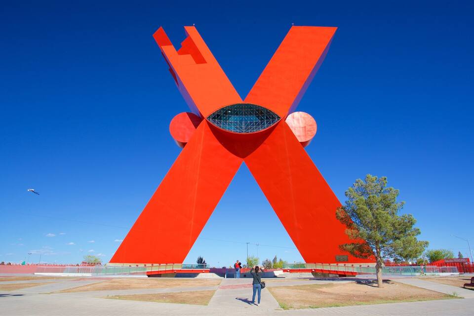 A large red X-shaped sculpture with a circular opening at the center, set against a clear blue sky.