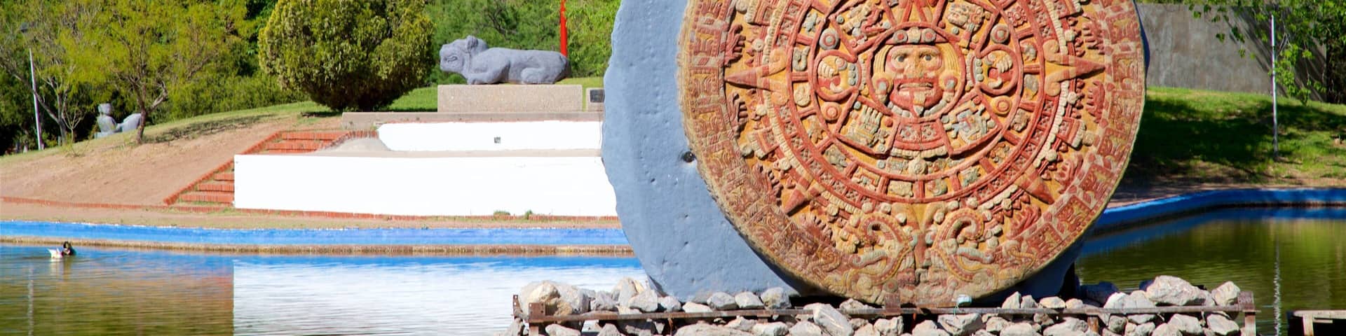 A large stone with intricate carvings, a body of water, and a statue of a creature.