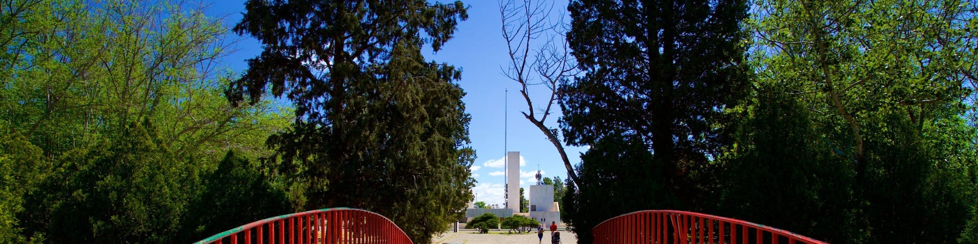 Un sendero adoquinado con barandillas rojas, rodeado de árboles y que conduce a un edificio con torre.