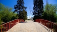 Un sentier pavé de pierres, bordé de rambardes rouges, entouré d’arbres et menant à un bâtiment doté d’une tour.
