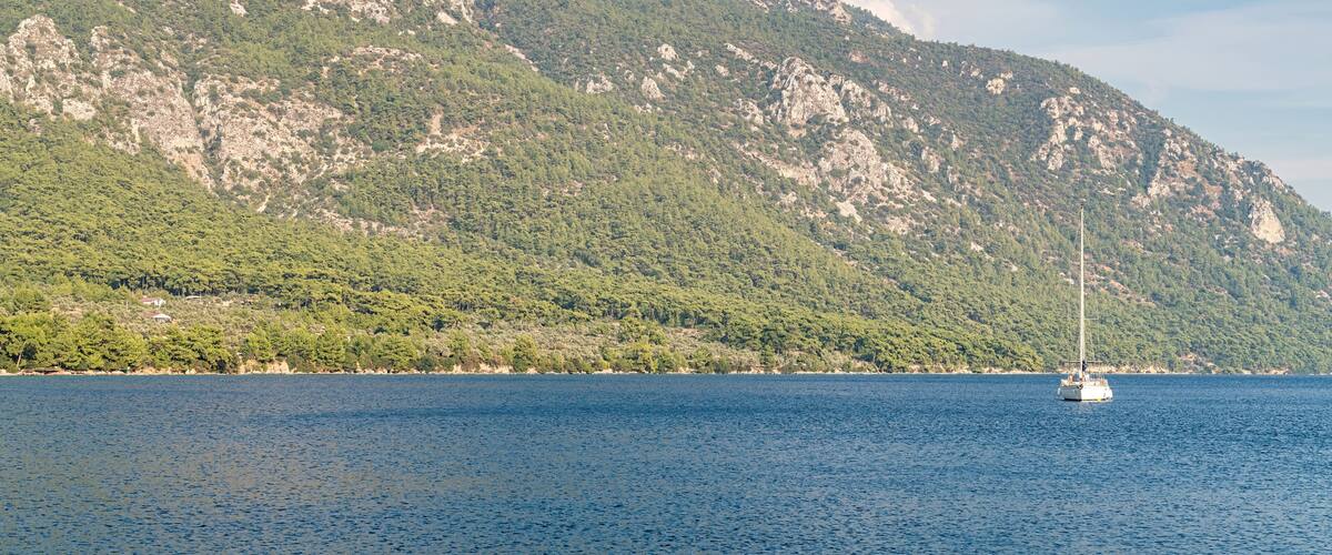 A sailboat on a calm sea with a mountainous coastline in the background.