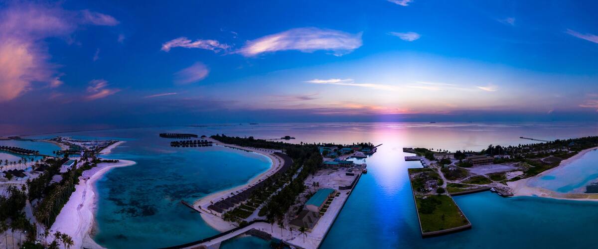 Ein tropisches Resort mit klarem türkisblauem Wasser, einer langen Pier und einem Sonnenuntergang über dem Ozean.