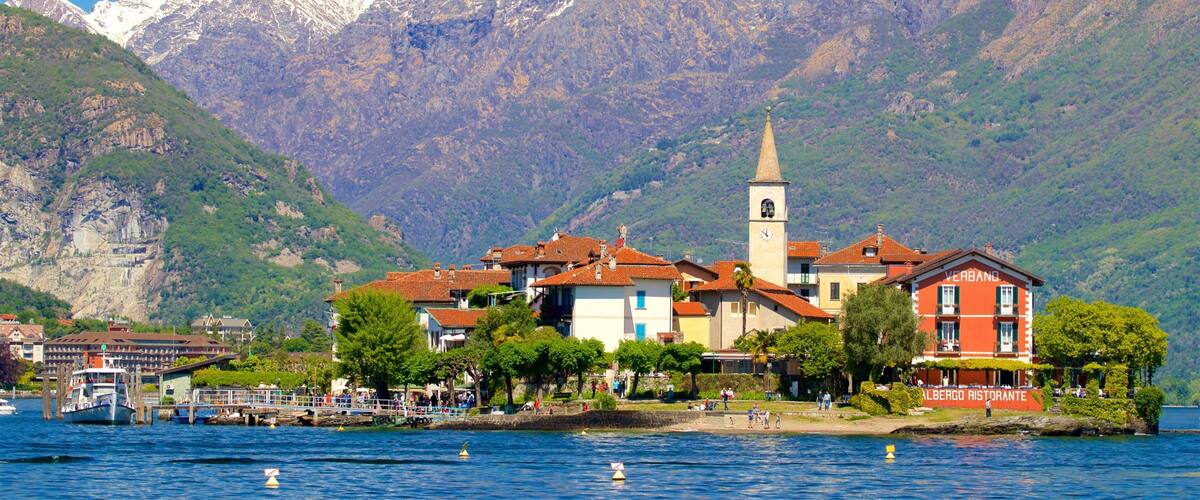A lakeside town with a prominent church tower, a restaurant named "Albergro Ristorante," and snow-capped mountains in the background.