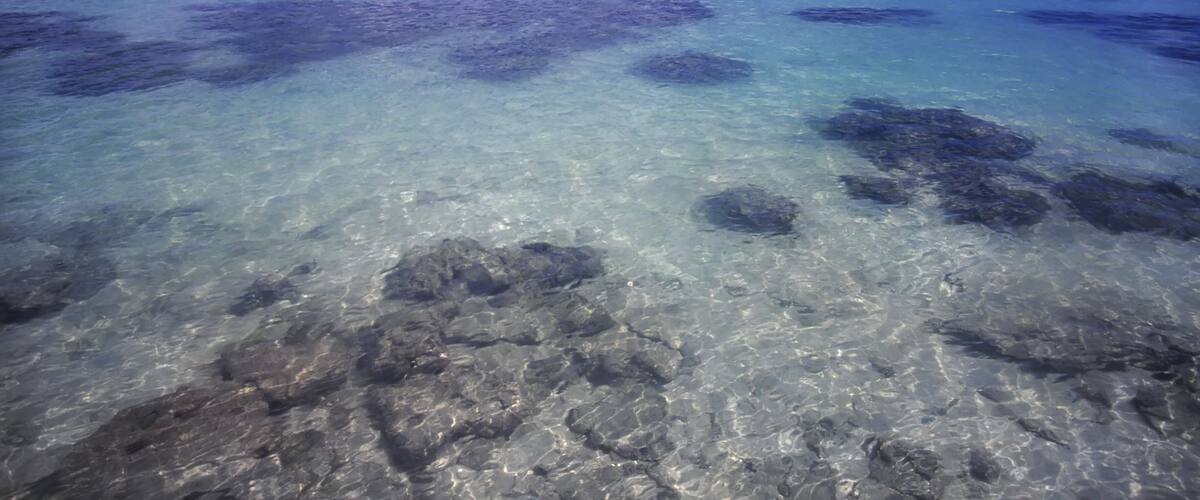 A clear blue sea with visible underwater rocks and a distant horizon.