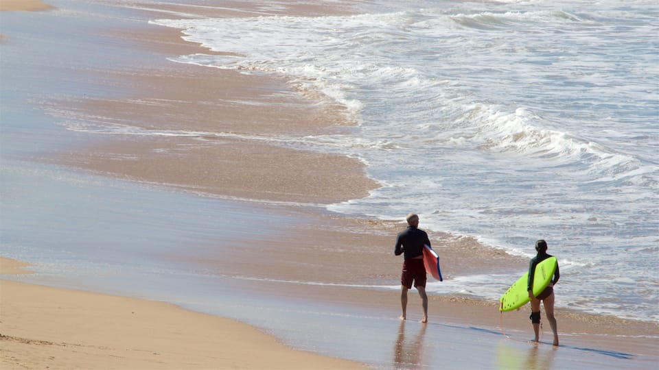 A beach with waves and two people carrying surfboards.