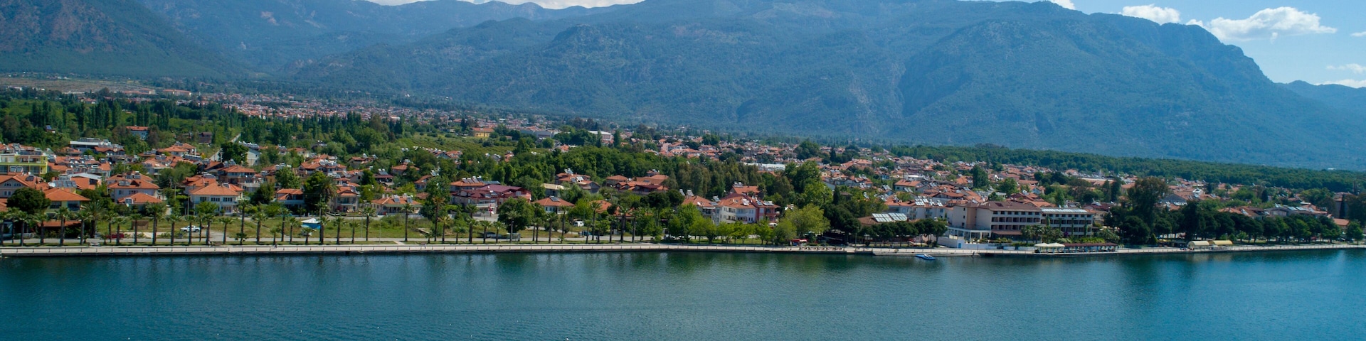 Un pueblo costero con un lago tranquilo, rodeado de montañas y edificios de techo rojo.