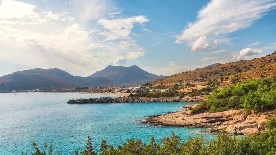 A coastal landscape with clear turquoise waters, rocky shores, and green vegetation.