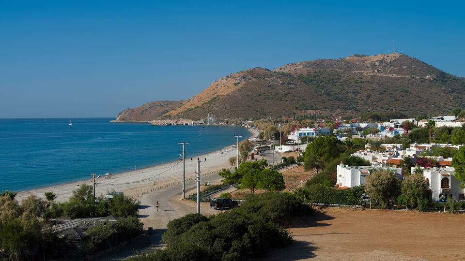 A coastal town with a beach, houses, and a hill in the background.