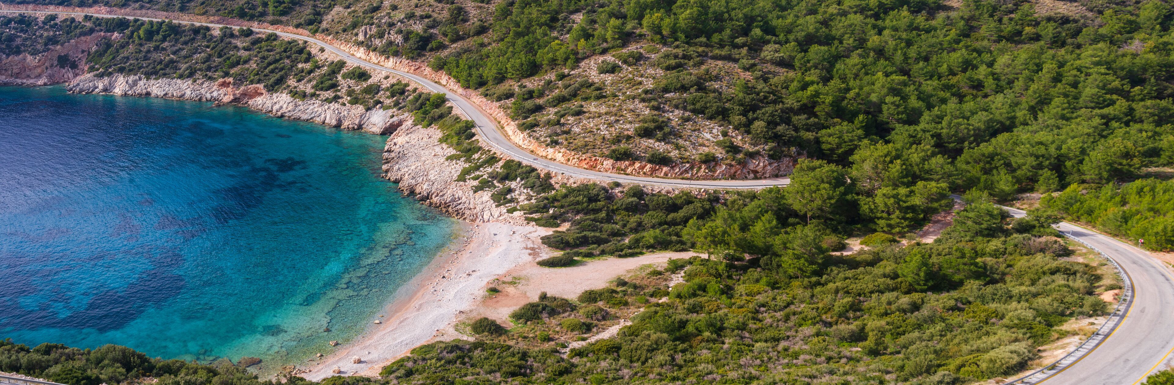 A coastal road winding through a forested area with a beach and turquoise waters.