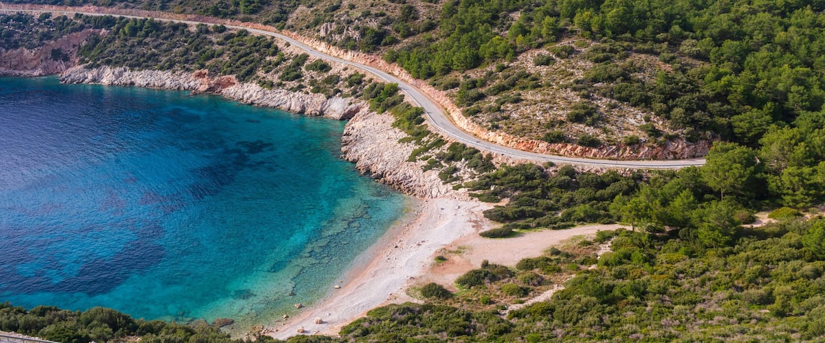 A coastal road winding through a forested area with a beach and turquoise waters.