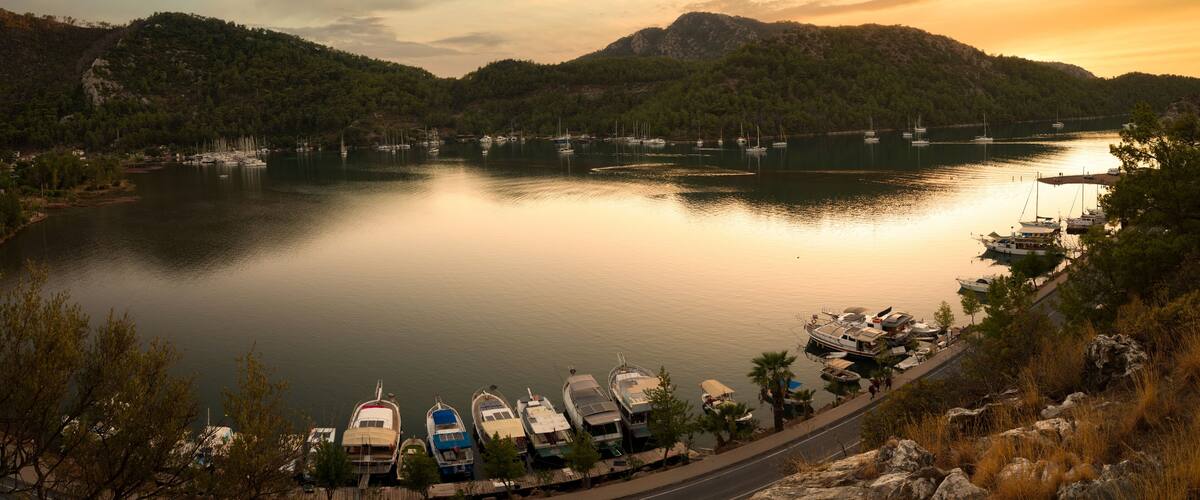 A calm lake with boats docked along the shore, surrounded by hills and trees.