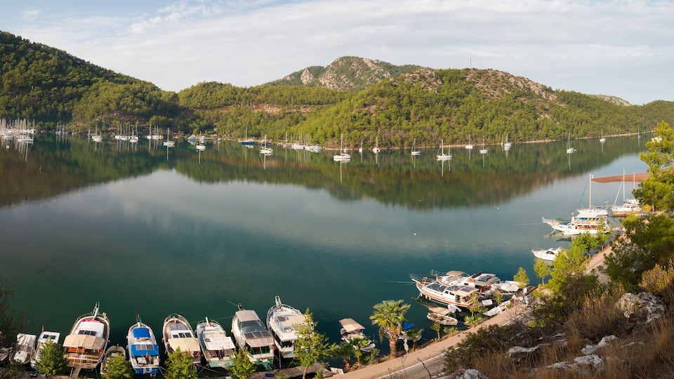 A calm lake with boats docked along the shore, surrounded by lush green hills.