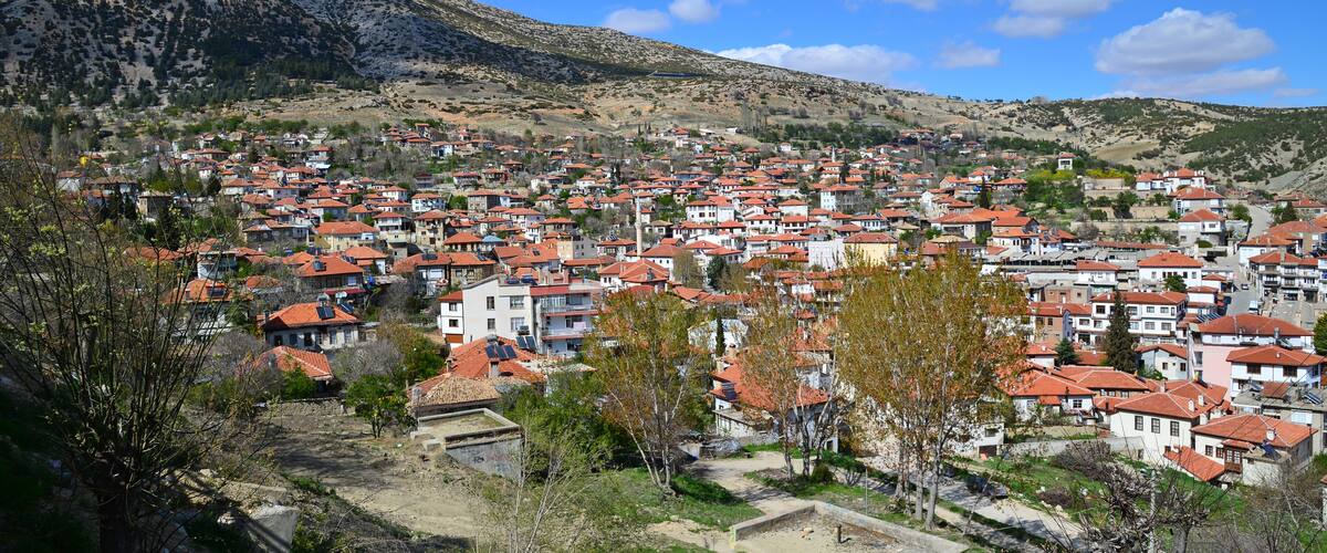 A town with red-roofed houses nestled in a valley with mountains in the background.