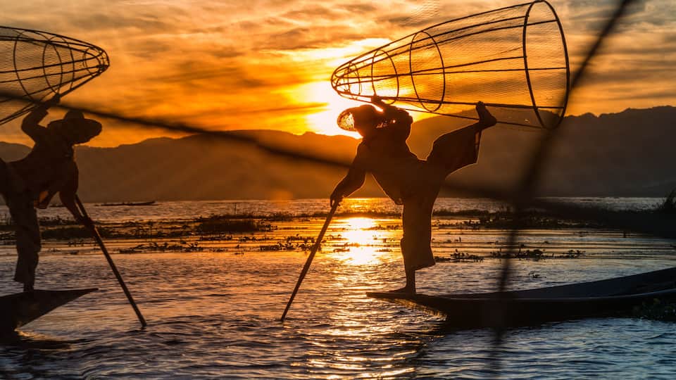Two people on a boat at sunset with fishing nets overhead.
