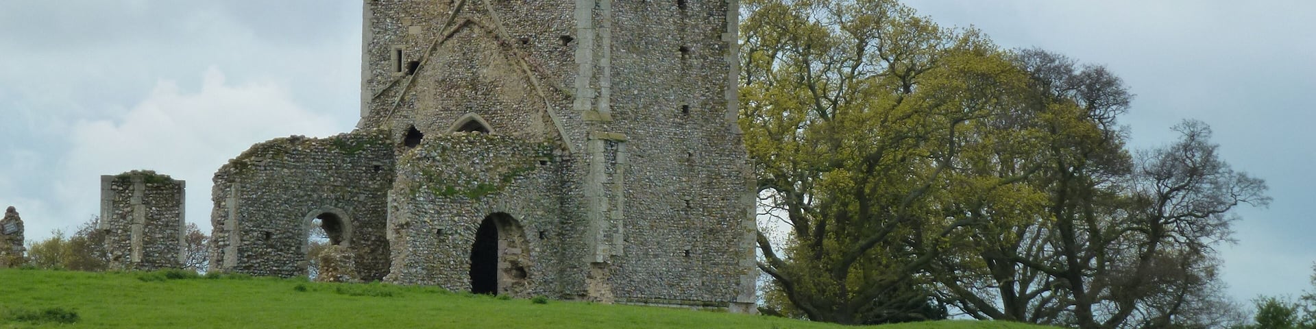 A medieval stone tower with arched windows and a grassy field in the foreground.