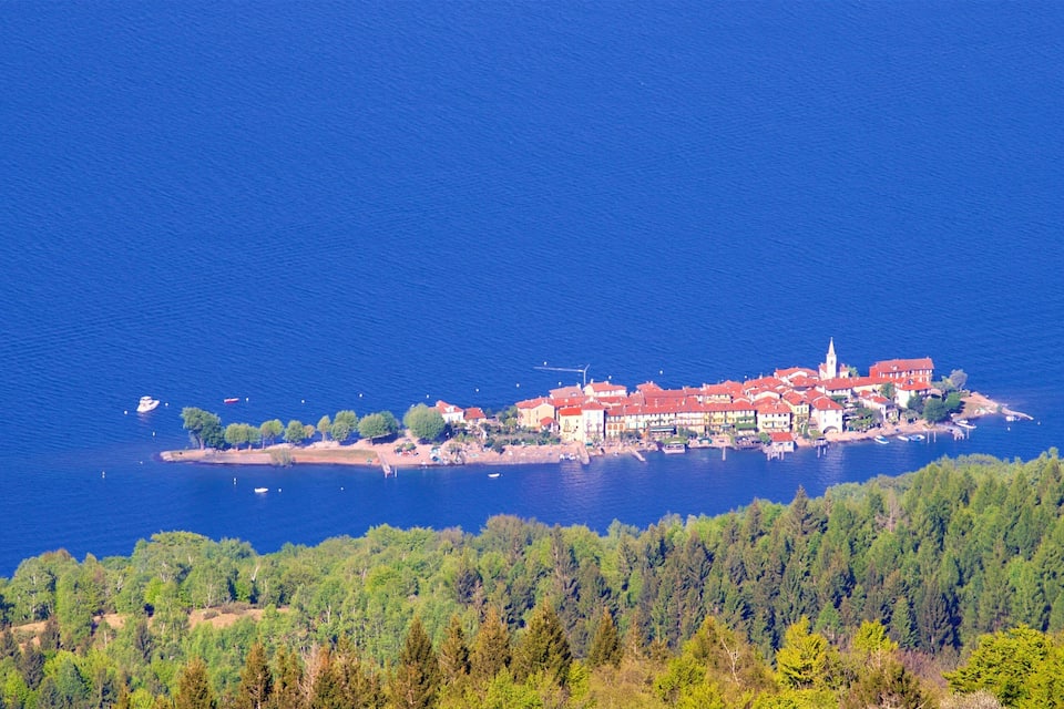 An aerial view of a coastal town with a prominent church, surrounded by dense forests and a clear blue sea.