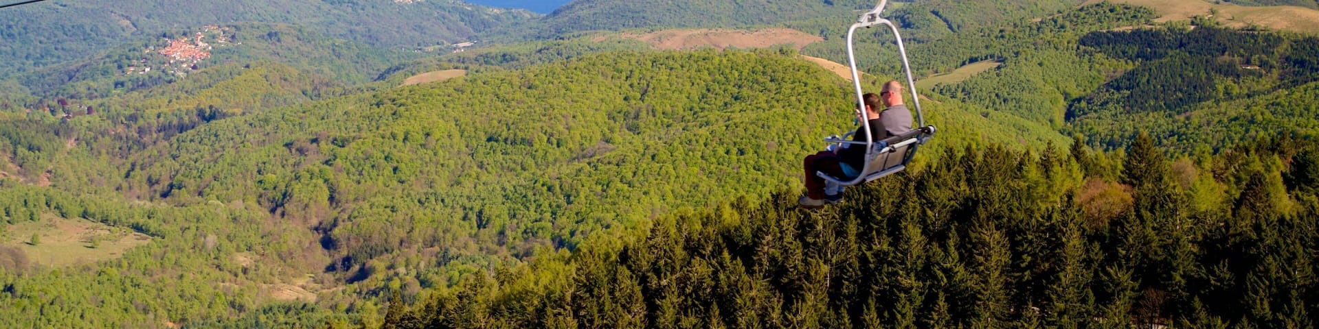 A cable car over a mountainous landscape with a lake in the distance.
