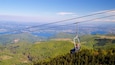 Eine Seilbahn über einer Berglandschaft mit einem See im Hintergrund.