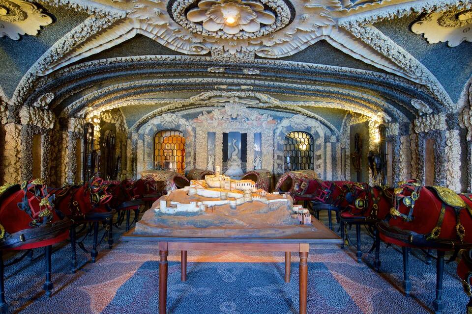 An ornate room with a long table, red chairs, and intricate ceiling decorations.