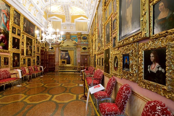 Ein prunkvoller Saal mit aufwendigen, goldenen Rahmen, roten, gemusterten Stühlen und einer reich verzierten Decke.