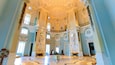 A grand hall with ornate ceilings, large windows, and classical columns.