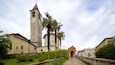 A historic church with a tall bell tower, palm trees, and a stone staircase leading to the entrance.