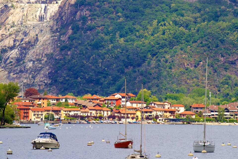 Une ville côtière avec des bâtiments aux toits rouges, une falaise rocheuse et plusieurs bateaux sur l’eau.