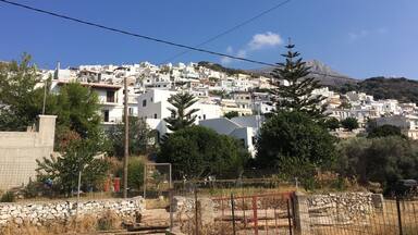 A coastal town with white buildings, a mountain in the background, and a clear blue sky.