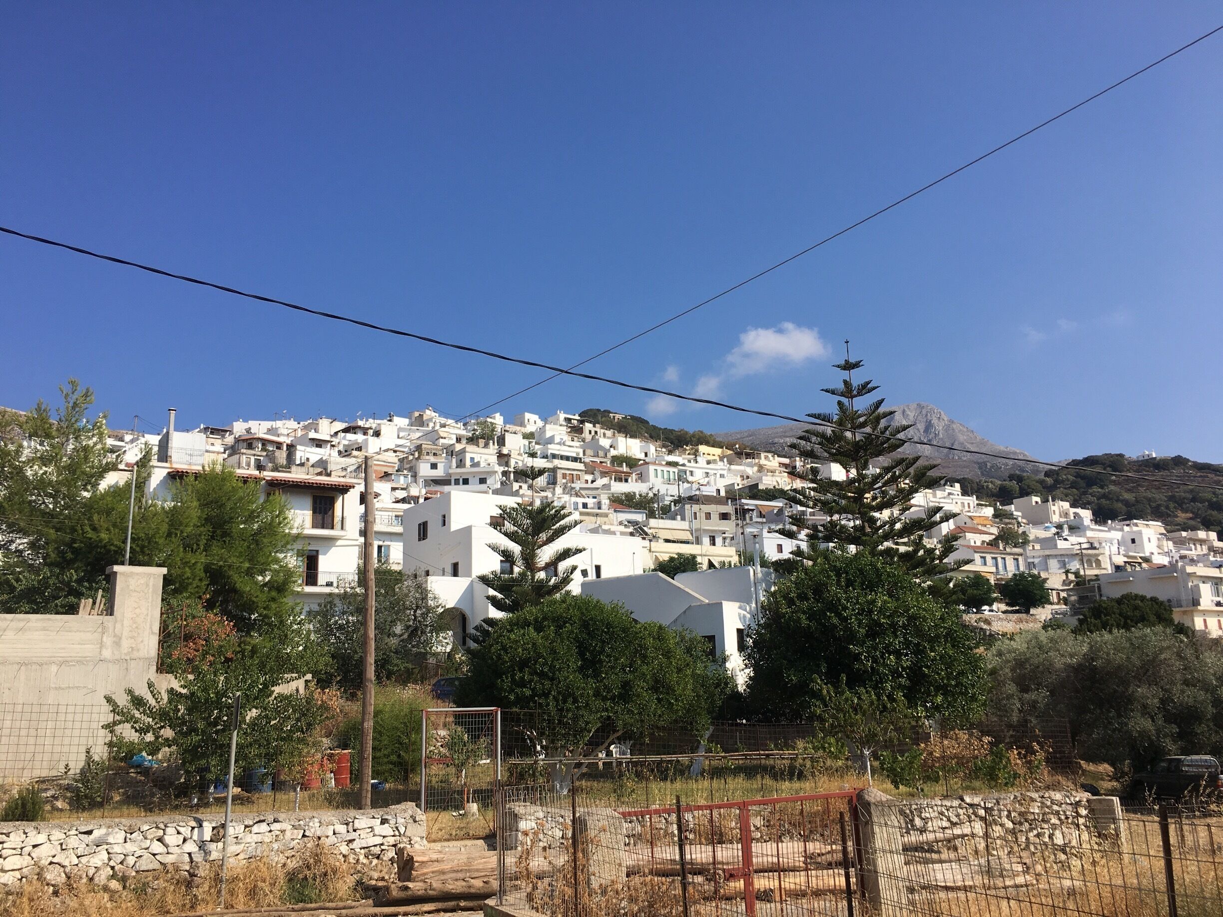 A coastal town with white buildings, a mountain in the background, and a clear blue sky.