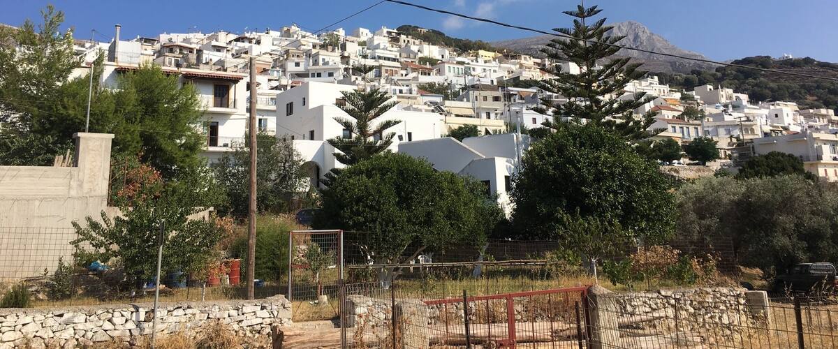 A coastal town with white buildings, a mountain in the background, and a clear blue sky.