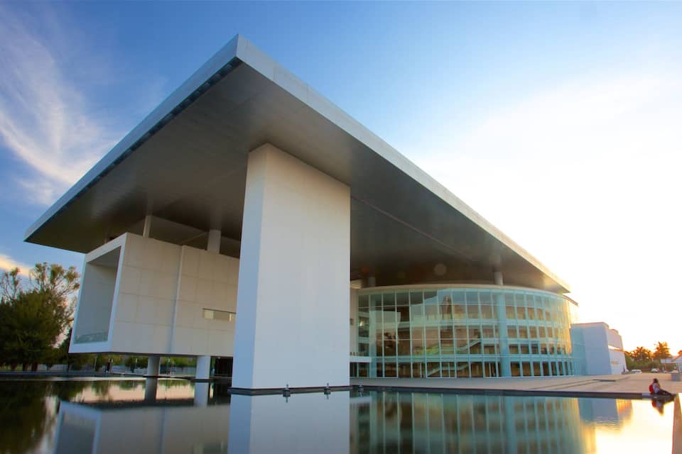 Um edifício de arquitetura moderna com uma grande cobertura saliente e uma piscina refletora à frente.