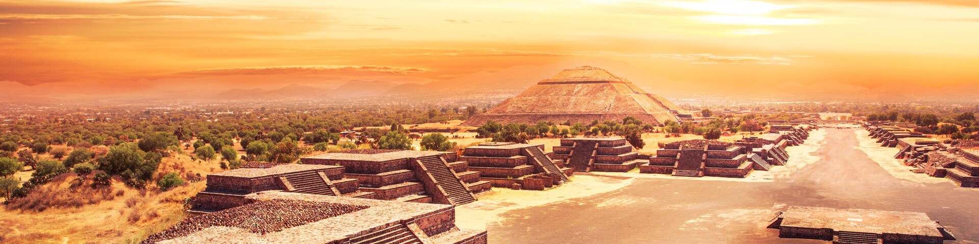 Ancient stepped pyramids, a large pyramid in the background, and a desert landscape at sunset.