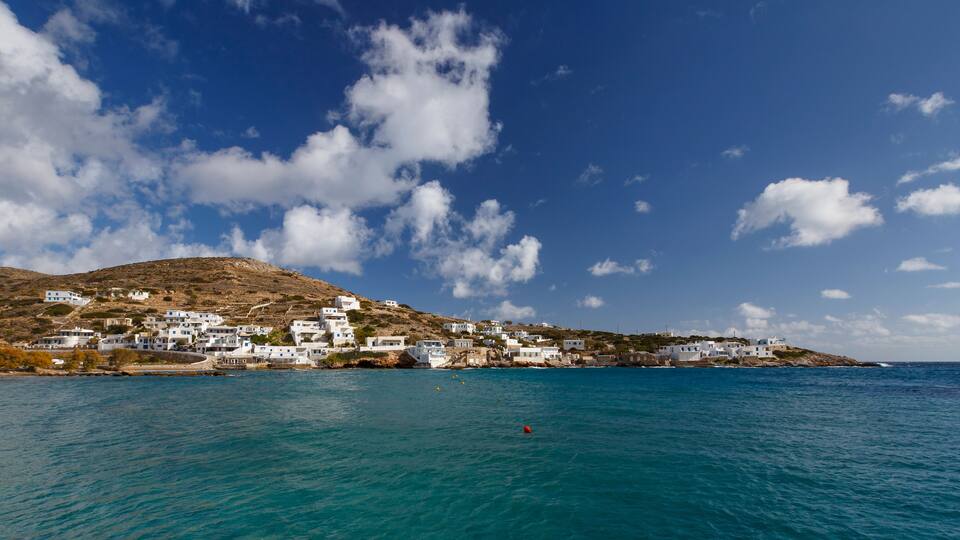 A coastal village with white buildings on a hillside, a clear blue sky, and calm sea.