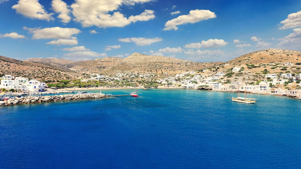 A coastal town with white buildings, a clear blue sea, and mountains in the background.
