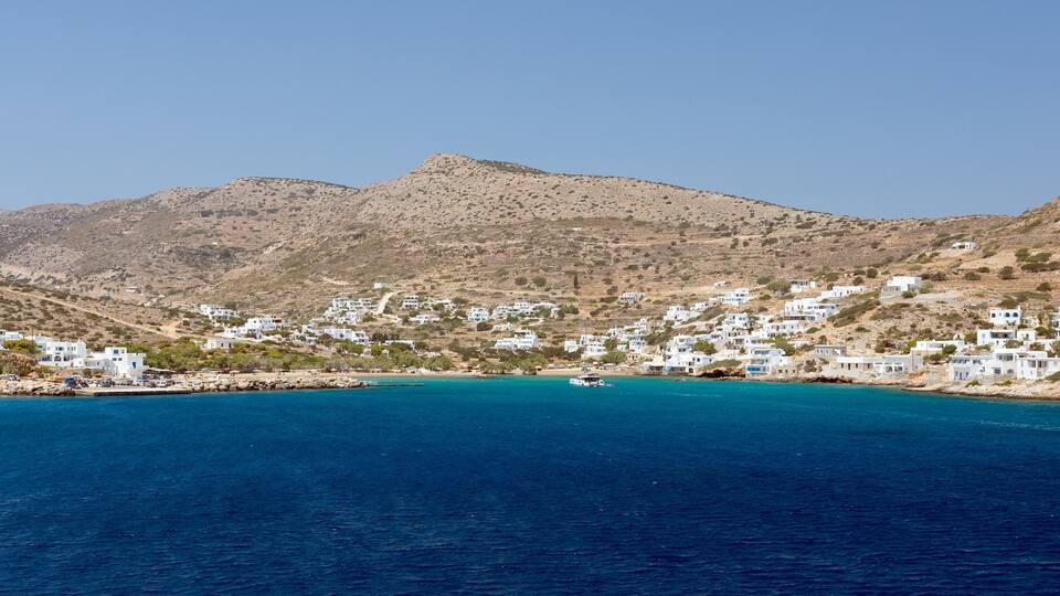 A coastal village with white buildings nestled against a backdrop of mountains.