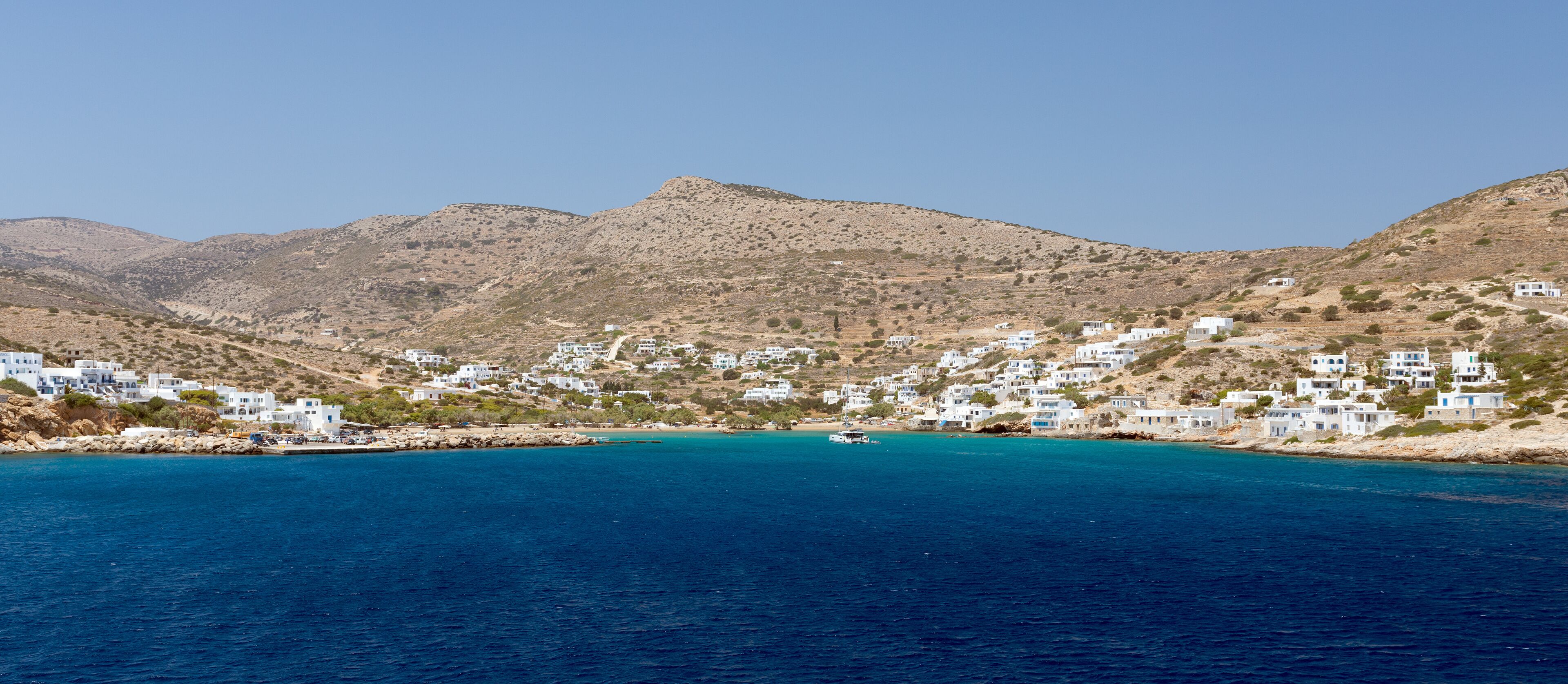 A coastal village with white buildings nestled against a backdrop of mountains.